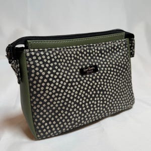 May include: A small, rectangular pouch with a black and white polka dot pattern on the front. The sides and top are olive green. The pouch has a black zipper and a small label that reads "Give Thanks Boutique."