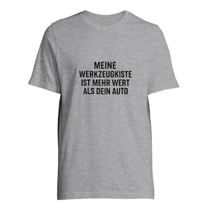 Könnte beinhalten: Hellgraues T-Shirt mit dem schwarzen Text "MEINE WERKZEUGKISTE IST MEHR WERT ALS DEIN AUTO". Das Shirt hat kurze Ärmel und einen Rundhalsausschnitt.