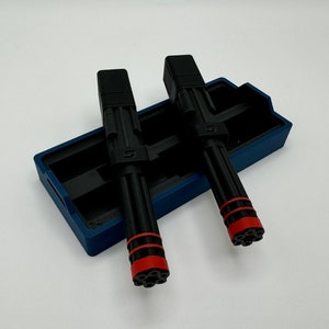 May include: Two black and red pens with a blue plastic case. The pens have a black body with a red tip and a black cap. The case has a blue exterior and a black interior.