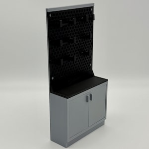May include: A grey cabinet with two doors and a black pegboard wall mounted above. The cabinet has a black countertop.