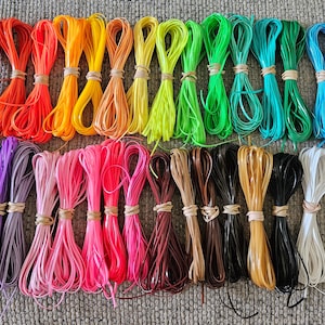 May include: A collection of colorful cords, arranged in rows, with a variety of colors including red, orange, yellow, green, blue, purple, pink, brown, black, and white.