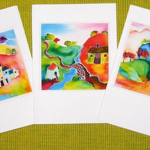 May include: Three watercolor paintings on white card stock. The first painting depicts a small village with colorful houses and a blue river. The second painting shows a green valley with a winding path and a small red house. The third painting features a blue mountain with green hills and red trees.