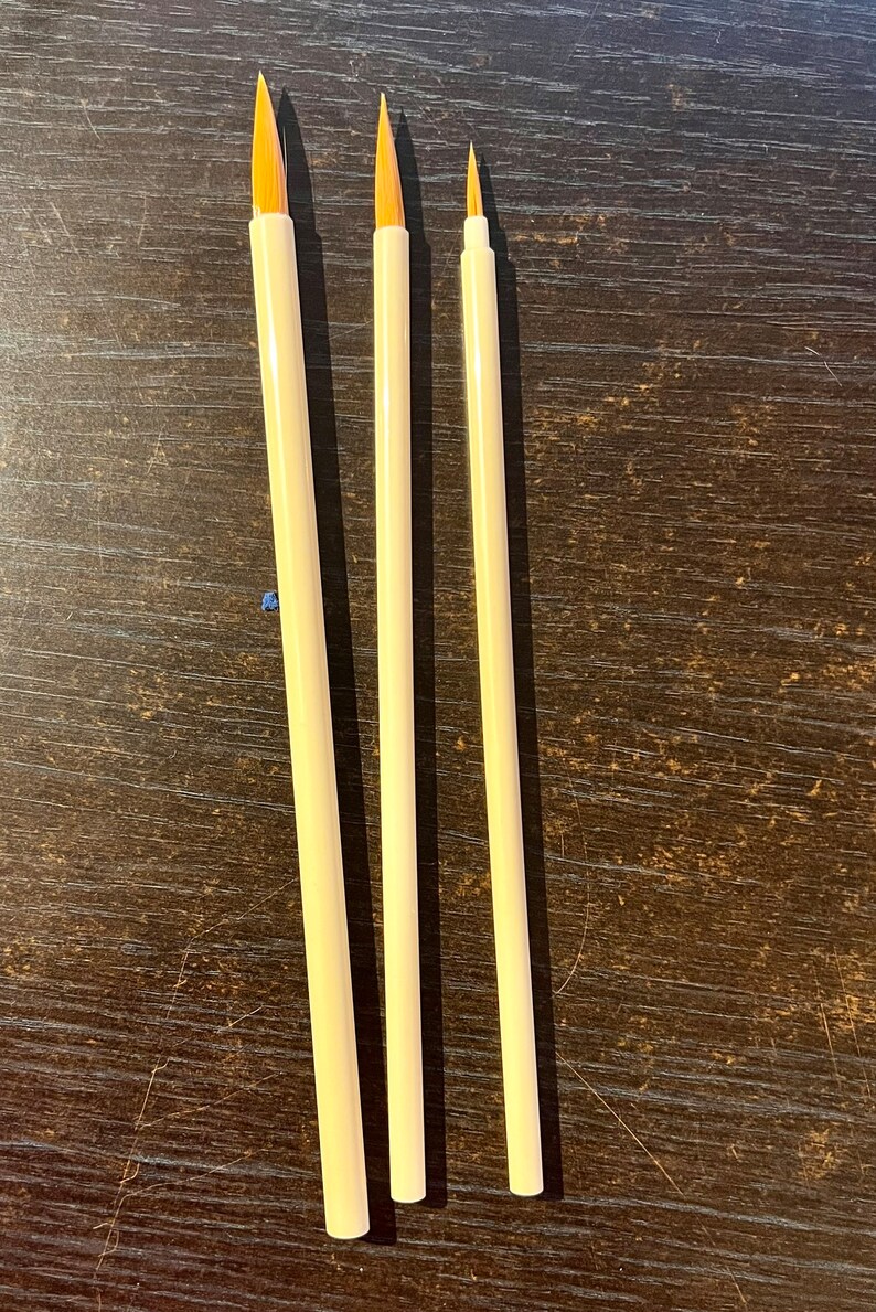 May include: Three paint brushes with wooden handles and natural bristles. The brushes are different sizes, with the largest brush on the left and the smallest brush on the right.