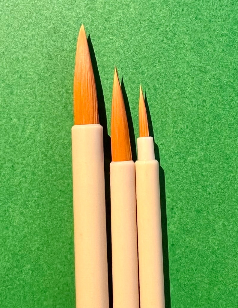 May include: Three paintbrushes with white handles and natural bristles of varying sizes. The brushes are arranged in order of size, with the largest brush on the left and the smallest brush on the right. The brushes are set against a green background.