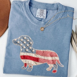 Blue Jean Comfort Colors patriotic dachshund patchwork t-shirt for women, featuring a large quilted wiener dog graphic with embroidered white stars, denim blue, red gingham, cream floral, and striped fabric — 4th of July dachshund mom gift, American flag wiener dog tee, cute dog mom patriotic shirt, patchwork dachshund Comfort Colors tee, dachshund lover gift idea.