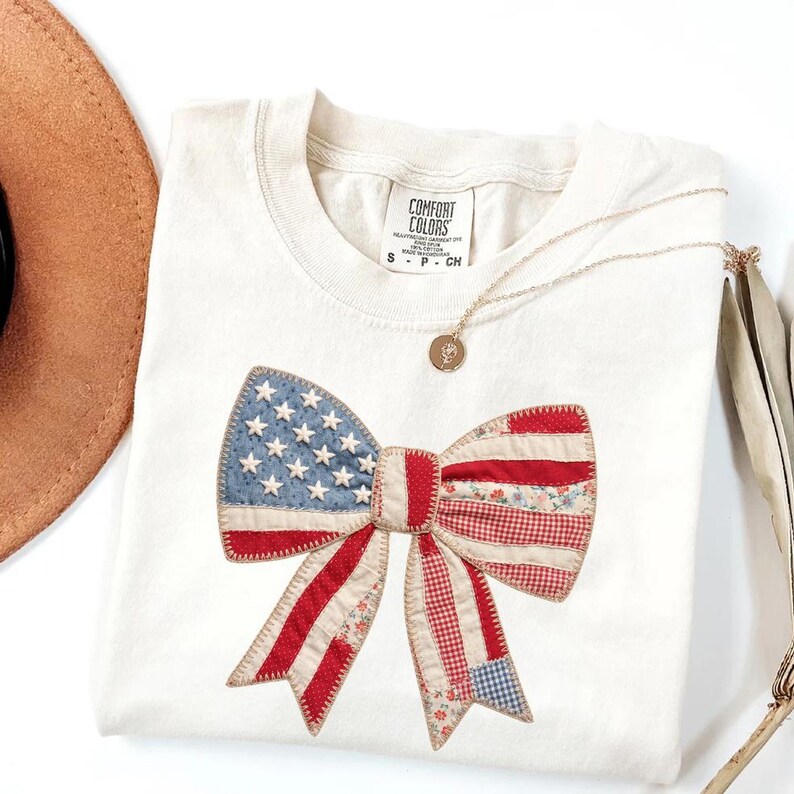 Ivory Comfort Colors patriotic bow patchwork t-shirt for women, featuring a large quilted bow graphic with embroidered white stars, red gingham, cream floral, and striped fabric — coquette 4th of July gift idea, American flag bow tee, cute patriotic shirt women, patchwork bow Comfort Colors shirt.