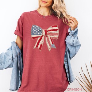 Ivory Comfort Colors patriotic bow patchwork t-shirt for women, featuring a large quilted bow graphic with embroidered white stars, red gingham, cream floral, and striped fabric — coquette 4th of July gift idea, American flag bow tee, cute patriotic shirt women, patchwork bow Comfort Colors shirt.