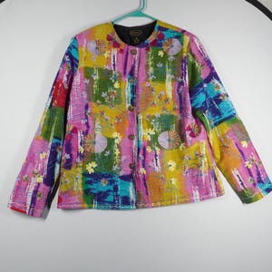 May include: A colorful, long-sleeved jacket with a vibrant patchwork design. The jacket features a mix of pink, yellow, blue, and green hues, adorned with floral embroidery and wooden buttons. The jacket is hanging on a green hanger.