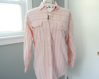 May include: A light pink button-down shirt with vertical white stripes. The long-sleeved shirt has two chest pockets and is displayed on a mannequin. The shirt has a collared neckline and button closures.