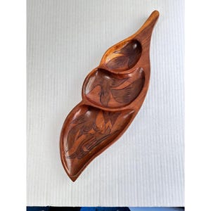 May include: A wooden serving tray with three carved compartments in a leaf shape. The tray is made of a dark brown wood and features intricate carvings of birds and foliage. The tray is approximately 18 inches long.