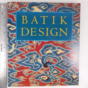 May include: A rectangular book titled BATIK DESIGN with a red, blue, and cream swirling pattern cover. A metal ruler is placed vertically along the left edge, showing the book height is approximately 11.75 inches and width is 9 inches.