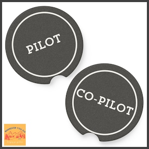 May include: Two round black coasters with white outlines and white text. The top coaster says "PILOT" and the bottom coaster says "CO-PILOT".