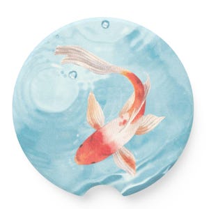 May include: A round blue and white coaster with a red and white koi fish swimming in the water. The fish has white fins and a red body with white spots.