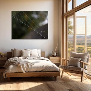 May include: A wooden bed frame with a white duvet and pillows. The bed is in a room with a large window and a wooden chair. A framed photograph of a spiderweb with water droplets hangs on the wall.
