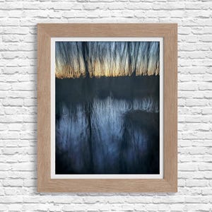 May include: A framed photograph of a dark blue and white abstract image. The image appears to be of a forest with trees reflected in a body of water. The trees are blurred and appear to be moving.