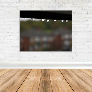 May include: A close-up of raindrops hanging from a gutter, with a blurred background of houses and trees.