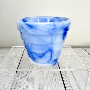 May include: A small, blue and white swirled glass planter. The planter has a tiered design and is made of a translucent material. The blue and white colors are swirled together, creating a marbled effect. The planter is empty.