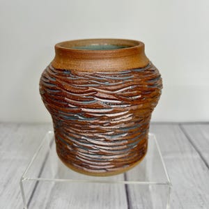 May include: A small, brown ceramic vase with a textured, wavy design. The vase has a light blue glaze on the inside.