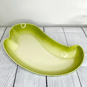 May include: A green ceramic serving dish shaped like a pepper. The dish has a light green interior and a darker green exterior.