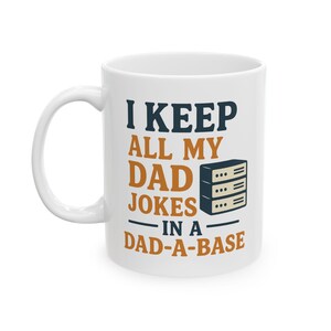May include: White ceramic coffee mug with the text "I KEEP ALL MY DAD JOKES IN A DAD-A-BASE" in navy blue and orange lettering. A graphic of a server rack is also on the mug. The mug has a white handle.