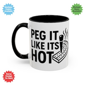 May include: White ceramic mug with a black interior, handle, and rim. The mug features the phrase "PEG IT LIKE ITS HOT" in bold black letters, along with a graphic of a peg and pegboard. The mug has a glossy finish.