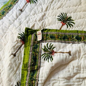 May include: White quilted bedspread with a green border and palm tree design. The border features a repeating pattern of green and brown elements. The palm trees have green fronds and red accents. The bedspread is folded, showing the pattern.