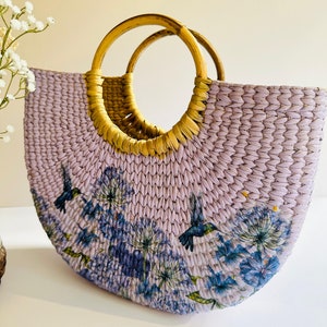 May include: A lavender woven tote bag with a floral print and two brown wooden handles. The print features blue hummingbirds and flowers.