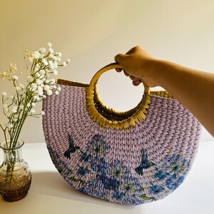 May include: A lavender woven tote bag with a wooden handle. The bag has a floral print with blue hummingbirds.