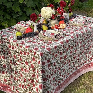 以下が含まれることがあります： 赤と緑の花柄の白いテーブルクロス。テーブルクロスは、花と果物のセンターピースが置かれたテーブルに敷かれています。テーブルには、皿、ナプキン、カトラリーが置かれています。