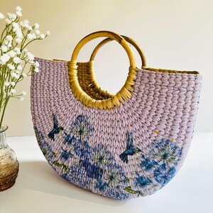 May include: A lavender woven tote bag with a floral and hummingbird print and two wooden handles.