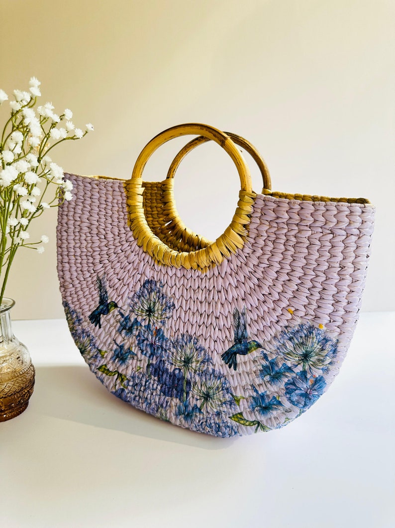 May include: A lavender woven tote bag with a floral and hummingbird print and two wooden handles.