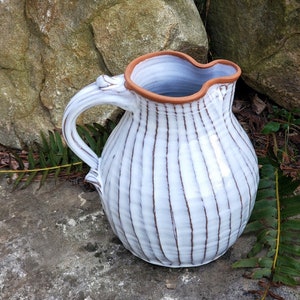 May include: White ceramic pitcher with brown stripes and a brown rim. The pitcher has a rounded body and a handle.