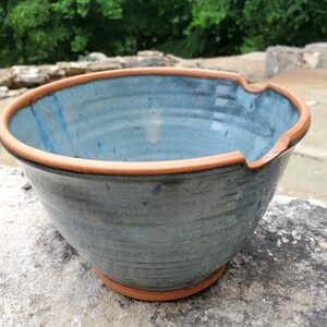 May include: A large, blue ceramic bowl with a brown rim. The bowl has a slightly uneven rim and a textured surface.