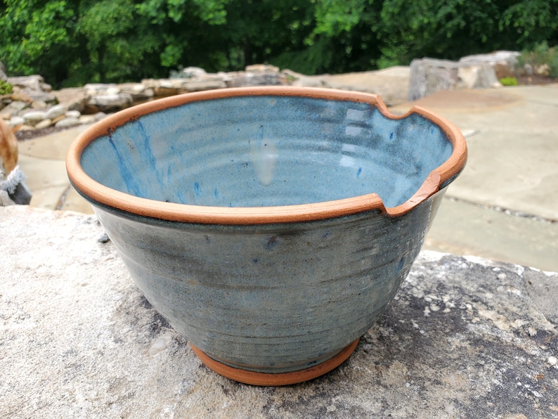 May include: A large, blue ceramic bowl with a brown rim. The bowl has a slightly uneven rim and a textured surface.