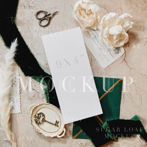 May include: A styled mockup scene featuring a white 9x4 inch card, cream-colored flowers, a vintage key on a decorative plate, and dark green velvet ribbon. Small scissors and an envelope are also present, all arranged on a textured beige surface.