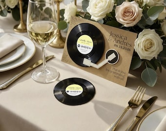 Könnte beinhalten: Eine beigefarbene Karte mit einer schwarzen Schallplattengrafik und einem Tonarm, bedruckt mit Jessica & Andres 08.18.2026 und Thank you for celebrating with us. Ein passender runder Schallplatten-Untersetzer liegt unterhalb der Karte auf dem Tisch.