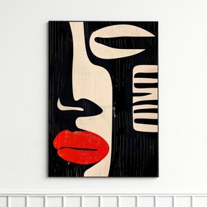 May include: A black and white abstract art print of a face with a red lip. The print is hanging on a white wall above a brown leather armchair and a black side table.