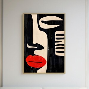 May include: A white couch with green pillows sits in front of a black and white abstract art print of a face with red lips. The couch is in a room with a white coffee table and a rug.