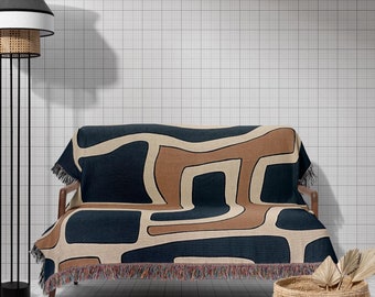 May include: A brown and blue patterned throw blanket with fringe on a couch with a black metal floor lamp with a white and black lampshade.