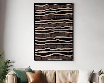 May include: A beige sofa with two pillows, a throw blanket, and a round wooden coffee table in front of it. A black framed print with a brown and white abstract pattern hangs on the wall behind the sofa.
