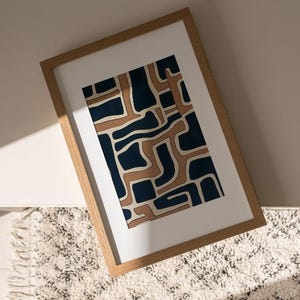 May include: A framed abstract print with a geometric pattern in shades of brown and blue. The print is in a wooden frame and is hanging on a wall.