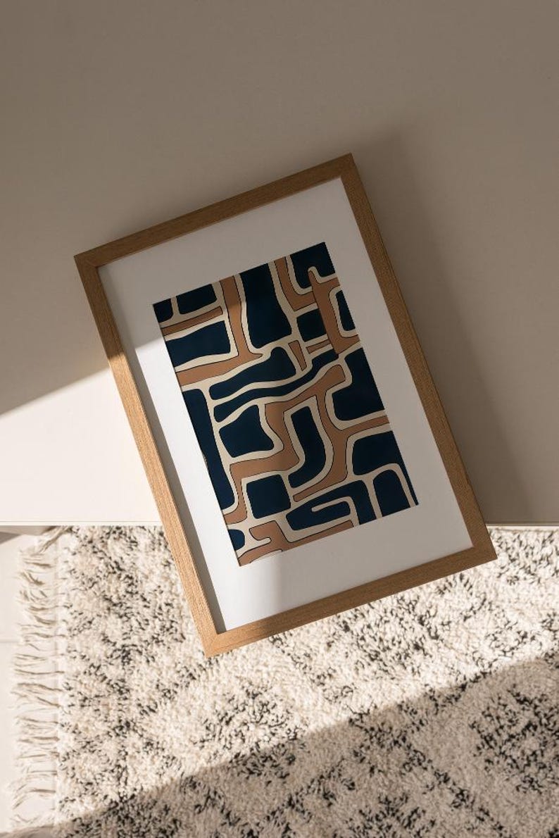 May include: A framed abstract print with a geometric pattern in shades of brown and blue. The print is in a wooden frame and is hanging on a wall.