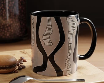 May include: A black ceramic mug with a white and black abstract design. The mug has a large handle and is sitting on a wooden surface.