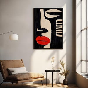 May include: Abstract art print featuring a black and white stylized face with a red lip. The print is framed and hanging on a white wall.