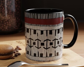 May include: A black ceramic mug with a white and black geometric pattern and a red band around the top. The mug has a black handle.