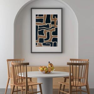 May include: A white round table with four wooden chairs. A framed abstract print with brown and blue geometric shapes hangs on the wall behind the table. A bowl of fruit sits on the table.