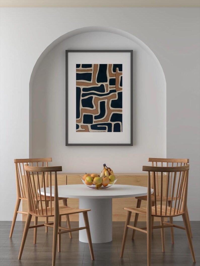 May include: A white round table with four wooden chairs. A framed abstract print with brown and blue geometric shapes hangs on the wall behind the table. A bowl of fruit sits on the table.