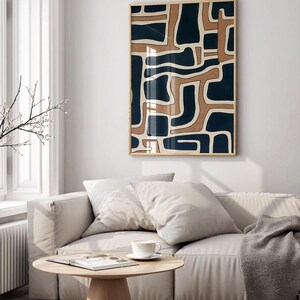 May include: A beige couch with two pillows and a gray throw blanket in front of a white wall with a framed abstract print featuring a geometric pattern of brown and blue shapes.