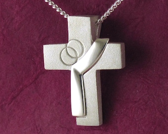 May include: Silver cross pendant necklace with a stylized ribbon design and two overlapping circles in the center.