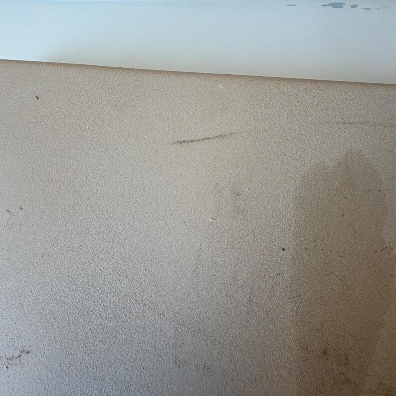 Puede incluir: Primer plano de una superficie texturizada de color beige claro con algunas marcas y motas oscuras. La superficie es ligeramente irregular y parece ser un material s&oacute;lido. Una superficie blanca es visible en la parte superior de la imagen.